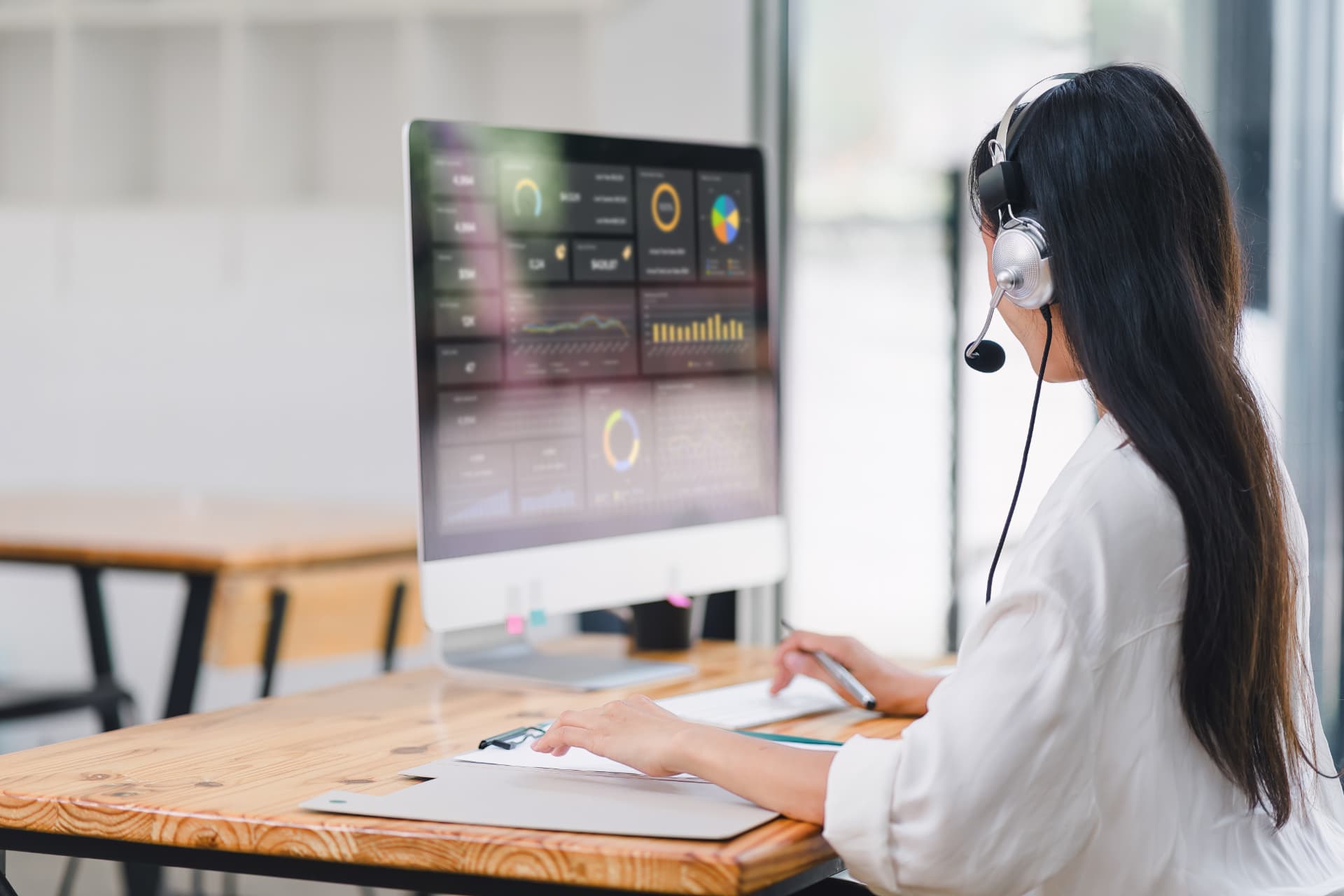 Contact centre advisor wearing a headset reviewing live performance dashboards on a desktop screen